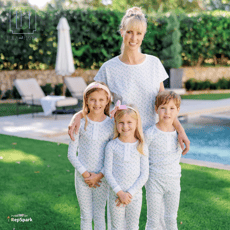 A woman and three young children standing near a pool on a beautiful sunny day wearing coordinating pajamas.