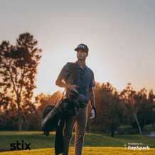 Man walking on a golf course with a golf bag on one shoulder at dawn.
