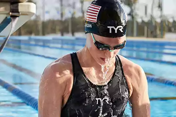 Photo of swimmer Claire Curzan wearing googles and a TYR swim cap breaking the top of the water.