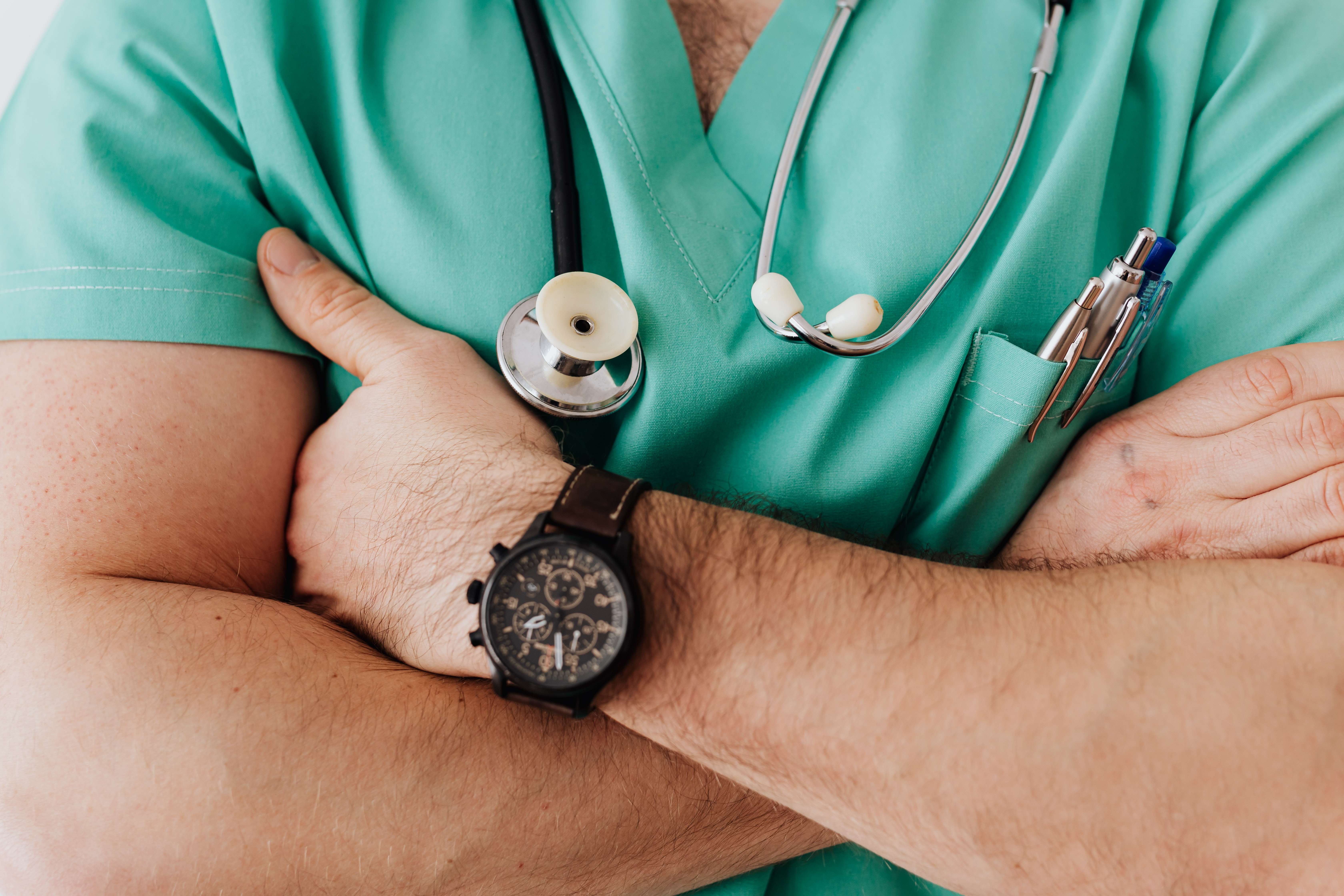 Zoomed in image of a male nurse in a turquoise scrub uniform crossing his arms over his chest.